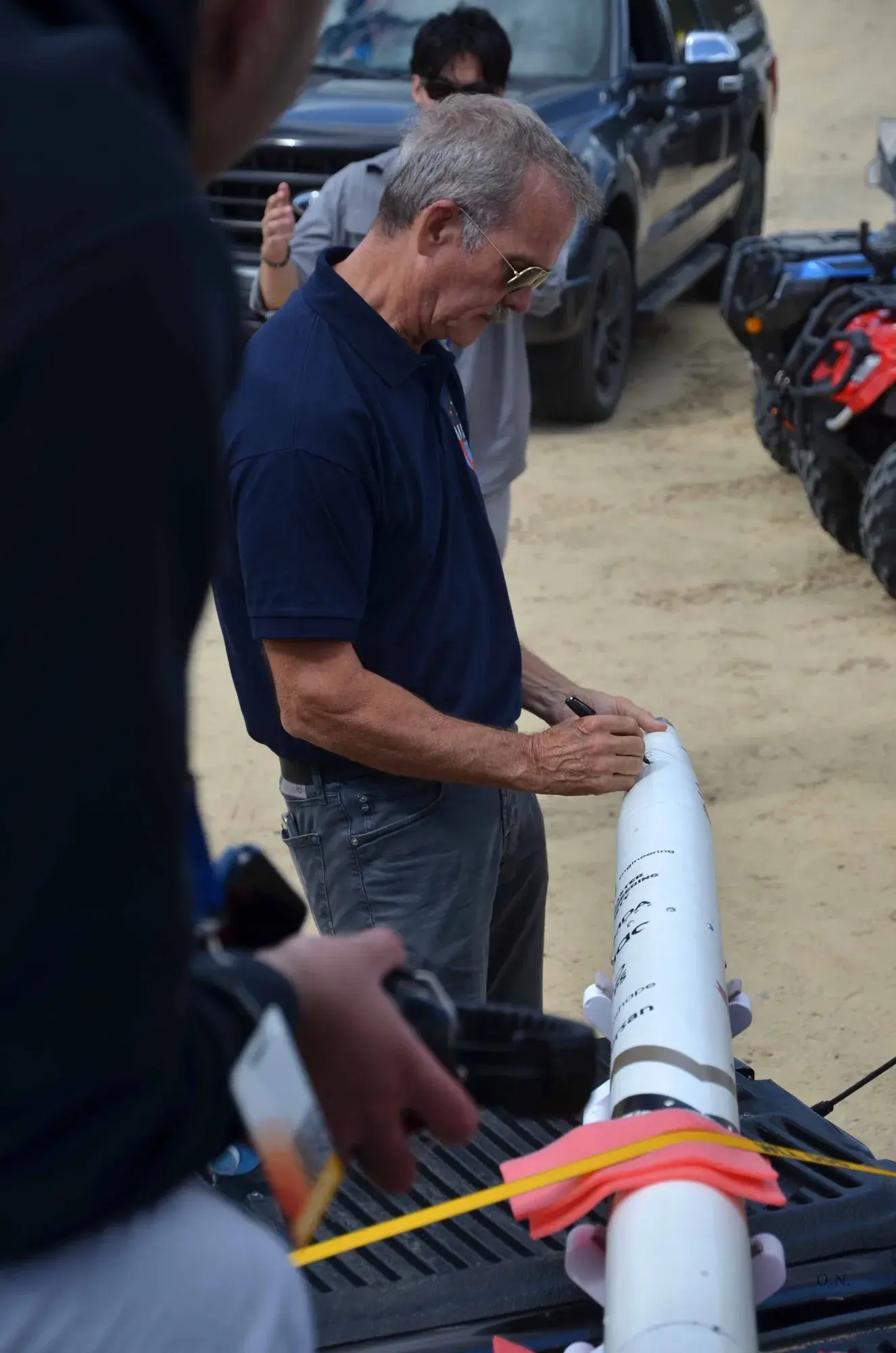 Chris Hadfield leans over Osiris's white nosecone on a truck tailgate and signs it with a black marker.