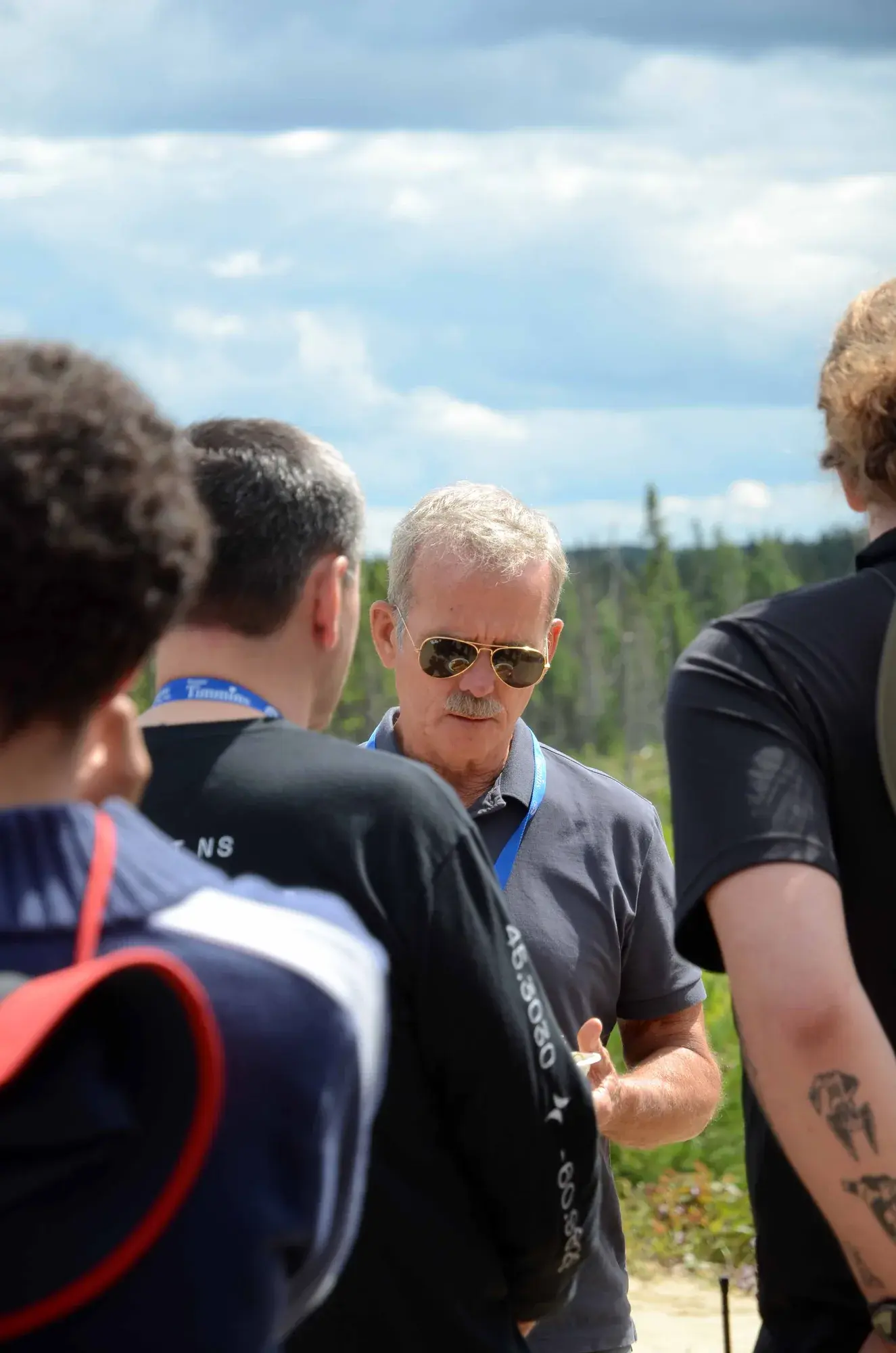 Chris Hadfield in aviator sunglasses and a grey polo, surrounded by McMaster Rocketry team members at the Launch Canada range.